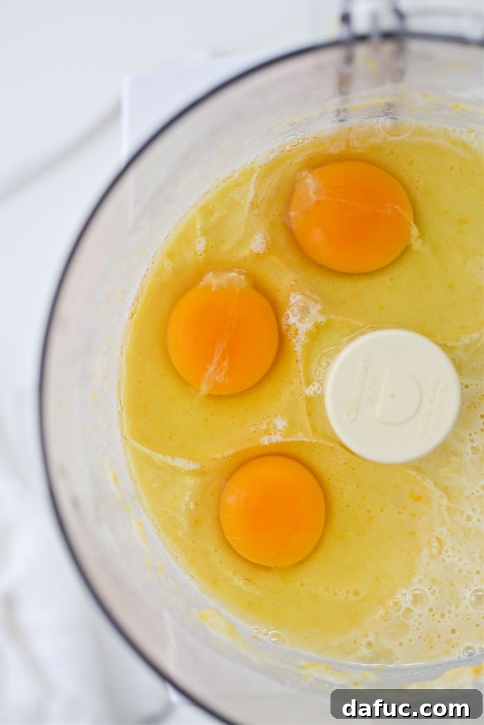 Adding three large eggs to the lemon filling mixture in the food processor