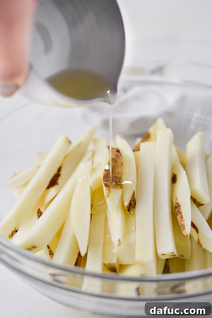 Golden Crispy Oven Fries 11 Dried potato fries drizzled with avocado oil in a mixing bowl.