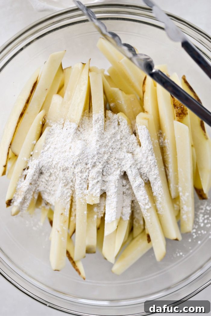 Golden Crispy Oven Fries 12 Potato fries being tossed with the seasoned cornstarch mixture in a bowl.