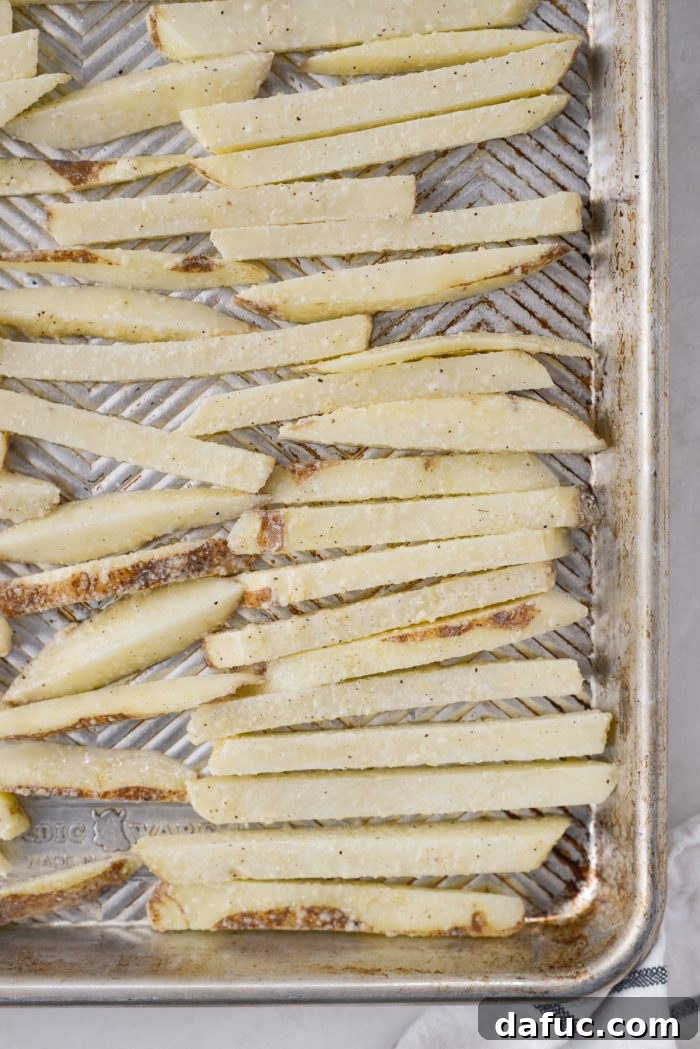 Golden Crispy Oven Fries 14 Oven baked French fries spread in a single layer on a hot baking sheet after the initial 15 minutes of baking.