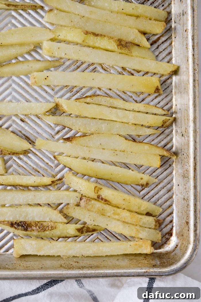 Golden Crispy Oven Fries 15 Close-up of oven baked French fries being turned with tongs on a baking sheet to ensure even crisping.