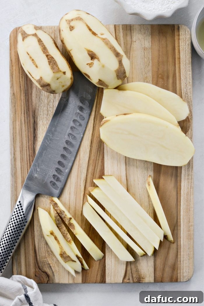 Golden Crispy Oven Fries 5 A cutting board with russet potatoes being sliced into even planks and then into thin French fry sticks.