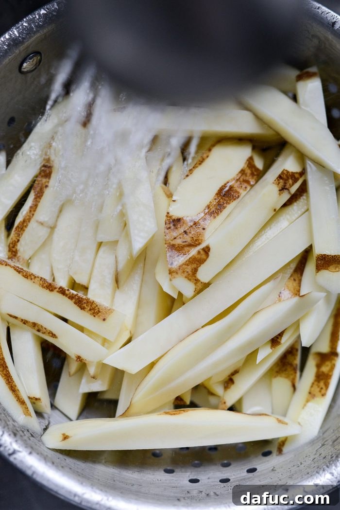 Golden Crispy Oven Fries 9 Freshly soaked potato fries being drained in a colander under running cold water.