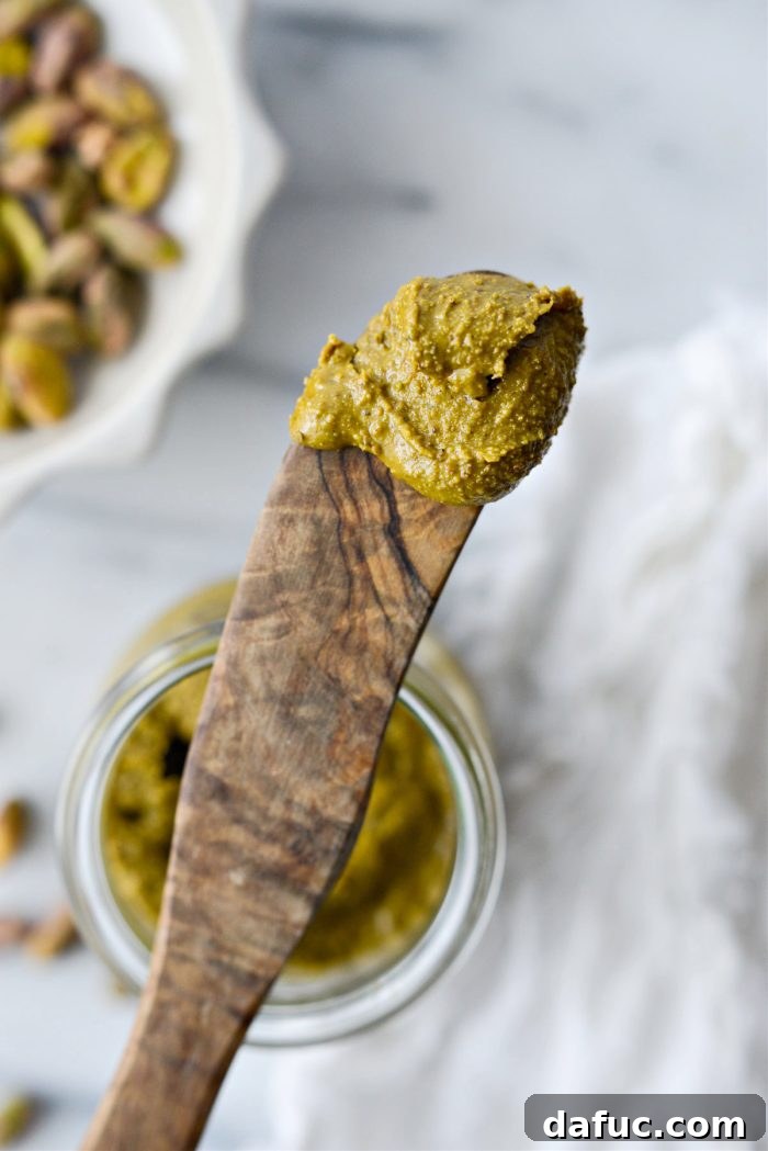 A wide shot of freshly made homemade pistachio butter in a jar, alongside whole pistachios.