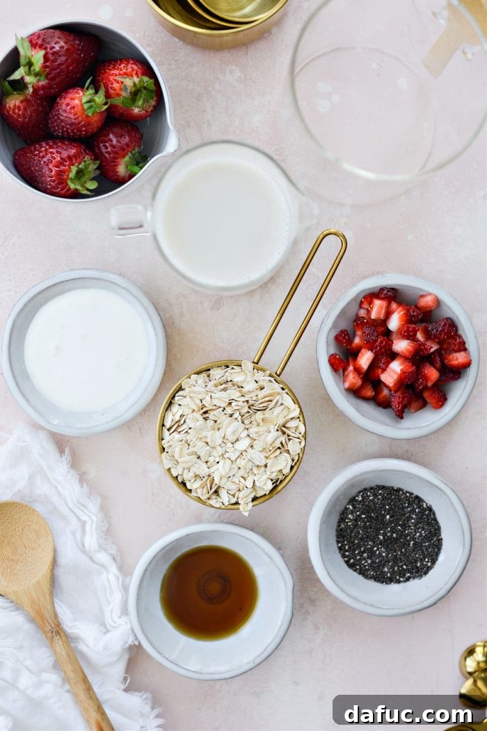 Creamy Strawberry Overnight Oats 4 A flat lay photograph displaying all the fresh ingredients needed for Strawberries and Cream Overnight Oats: rolled oats, chia seeds, milk, yogurt, and whole strawberries.