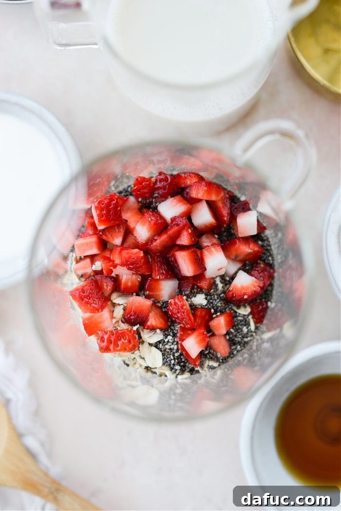 Creamy Strawberry Overnight Oats 5 A glass jar containing rolled oats, chia seeds, and diced strawberries, ready for mixing.