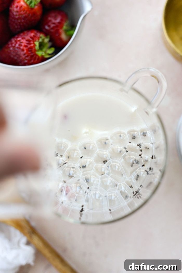 Creamy Strawberry Overnight Oats 7 Pouring unsweetened vanilla oat milk into the mixture of oats, fruit, yogurt, and syrup.