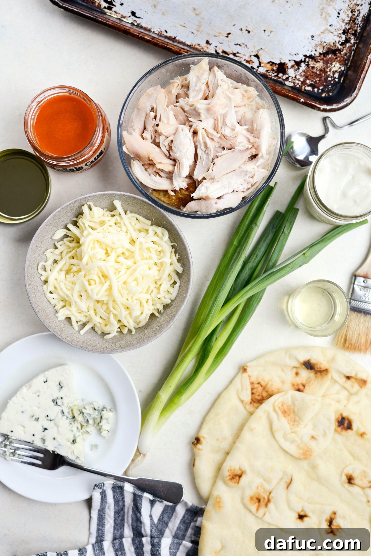 Ingredients for Buffalo Chicken Flatbread Pizzas laid out: naan, chicken, cheeses, buffalo sauce, green onions, and olive oil.