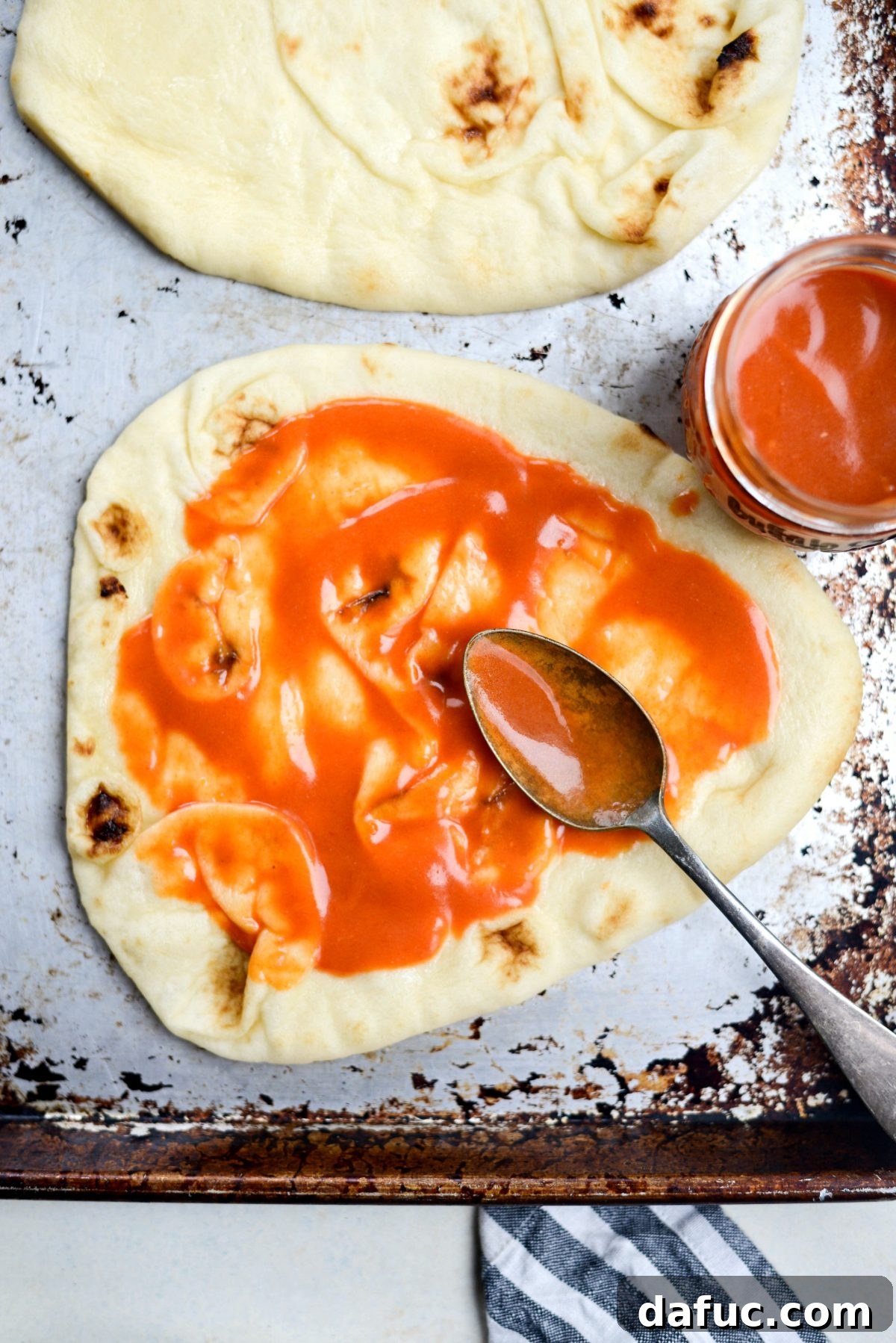 Naan bread fully spread with buffalo sauce, ready for toppings.