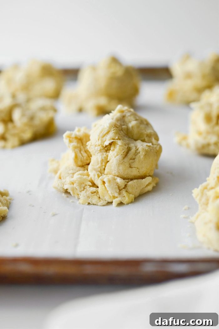 Effortlessly Fluffy Drop Biscuits 10 Mounds of easy homemade drop biscuit dough scooped onto a parchment-lined baking sheet.