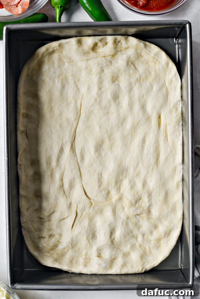 Focaccia pizza dough being stretched into an oiled baking pan