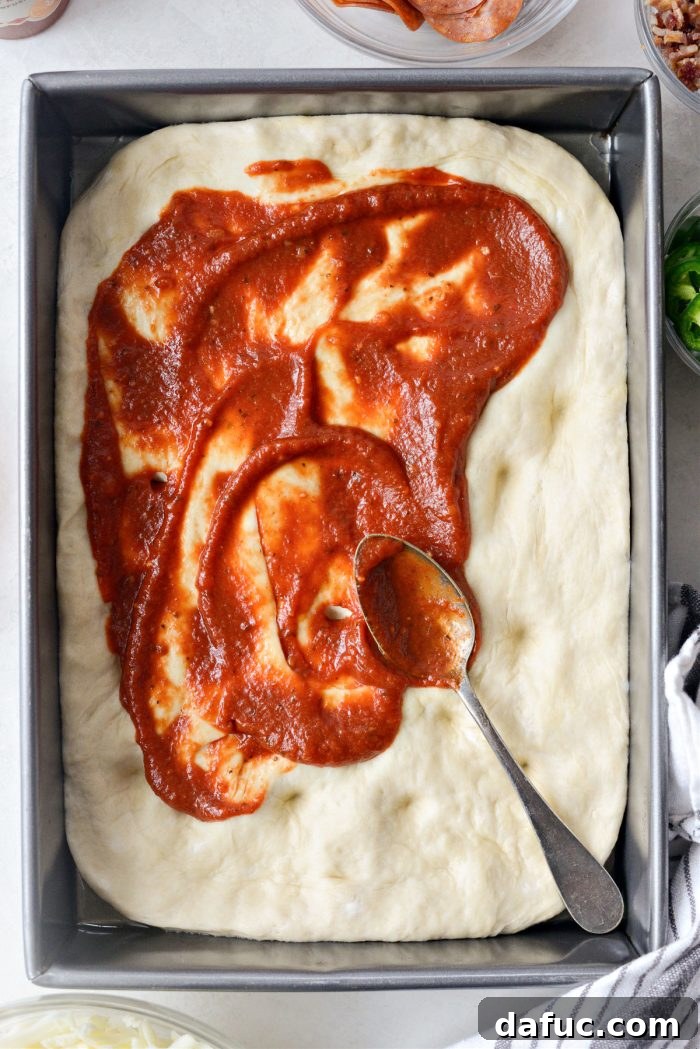 Pizza sauce being spread over focaccia dough