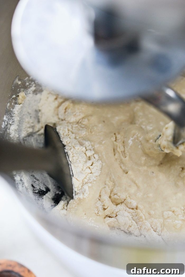 Fluffy Focaccia Pizza Dough Recipe 8 Stand mixer kneading dough, with a spatula nearby for scraping down the bowl.