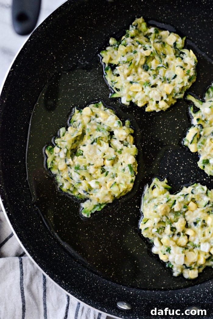 Crispy Zucchini Corn Fritters 12 A spatula gently pressing down on frying zucchini corn fritters to flatten them