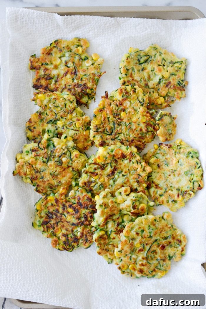 Crispy Zucchini Corn Fritters 14 Cooked Zucchini Corn Fritters resting on a paper towel-lined baking sheet