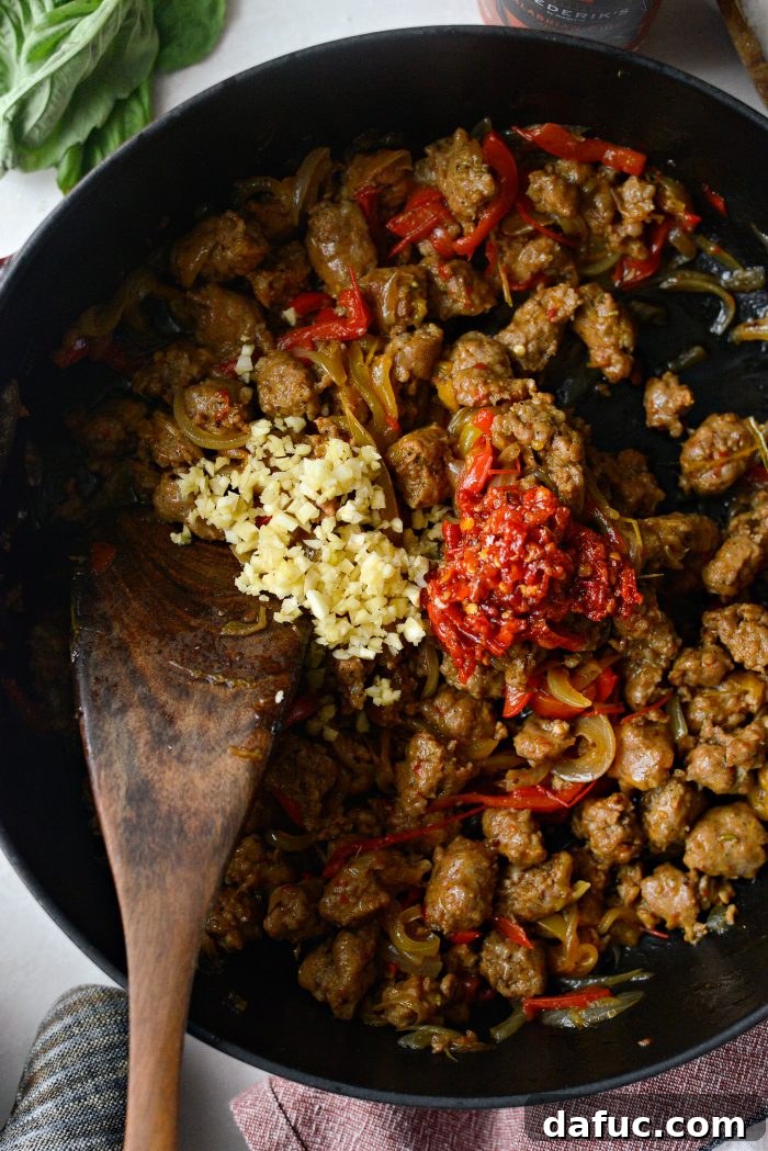 Minced garlic and Calabrian chili paste being added to the cooked sausage, peppers, and onions in the skillet.