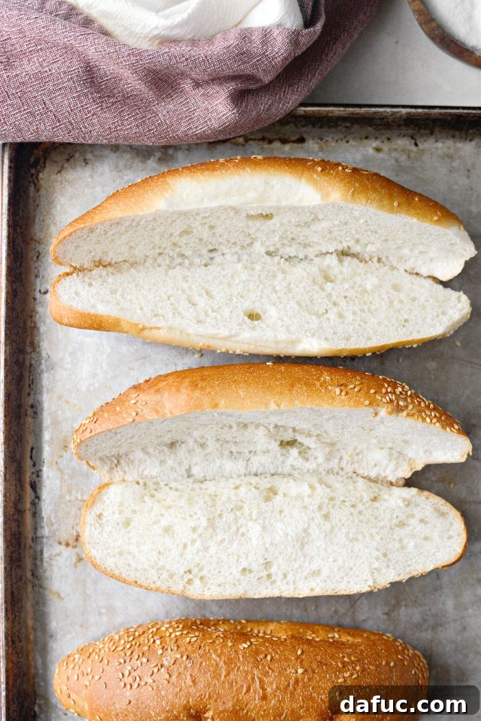 Four Italian sub buns, sliced open and placed on a baking sheet, ready for toasting in the oven.