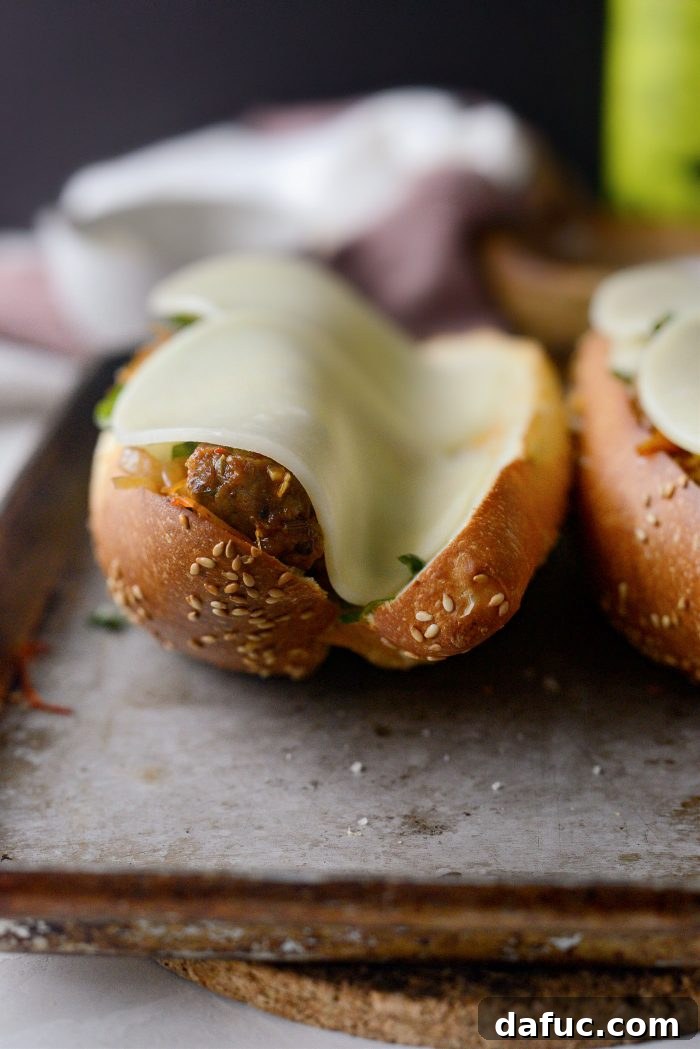 Two slices of provolone cheese neatly placed on top of the basil, Pecorino Romano, and sausage mixture in a sub.