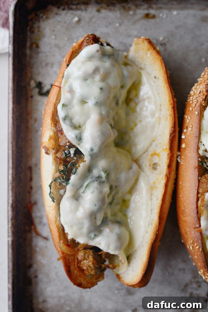 Spicy Italian Sausage Subs on a baking sheet under the broiler, with the provolone cheese visibly melted and slightly browned.