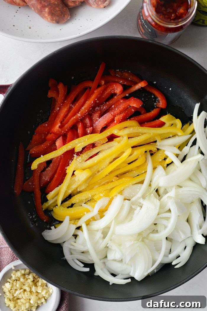 Sliced red and yellow bell peppers and onions cooking in a skillet with olive oil, showing them beginning to soften.
