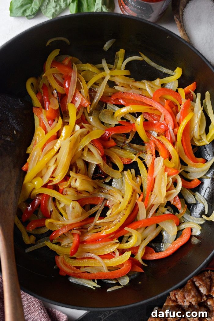 Slightly softened and translucent bell peppers and onions in the skillet, indicating they are ready for the next step.