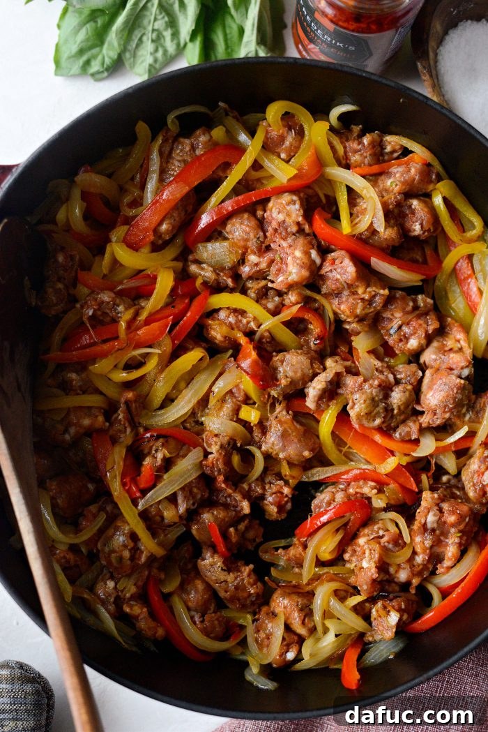 Chopped spicy Italian sausage added to the skillet with the softened peppers and onions, being stirred to combine.