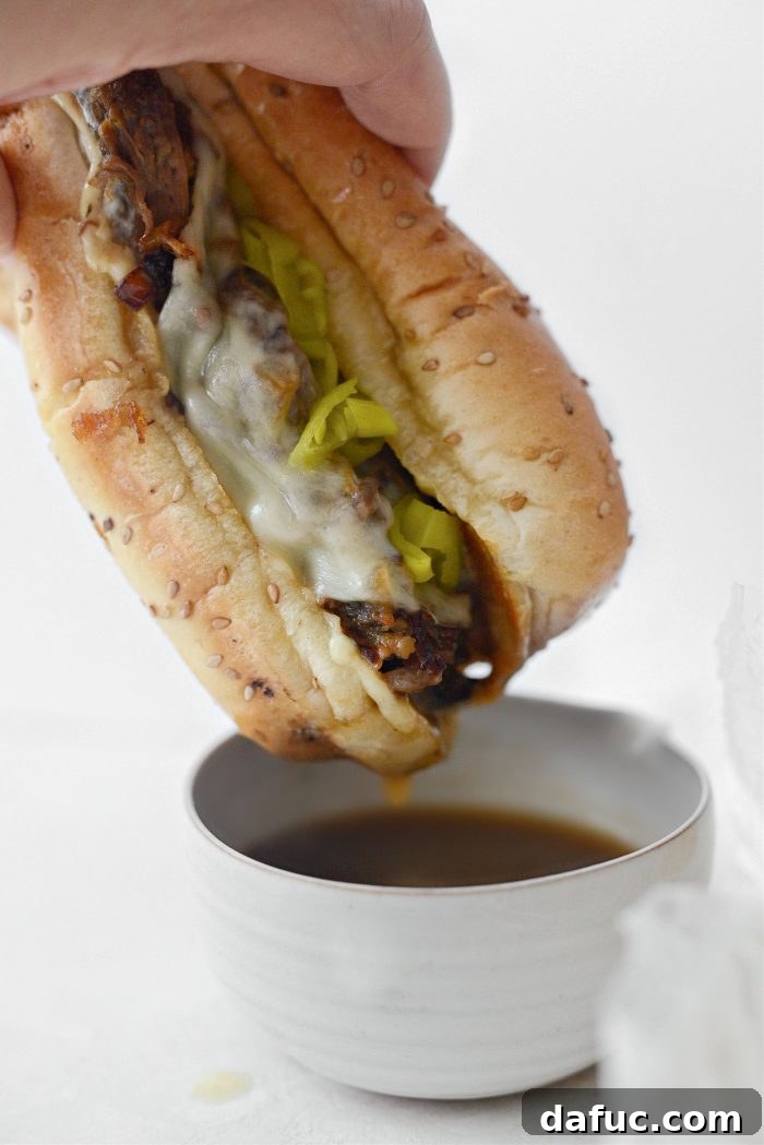 Close-up of a Mississippi Pot Roast Sandwich showing layers of meat, cheese, and onions, served with au jus for dipping.
