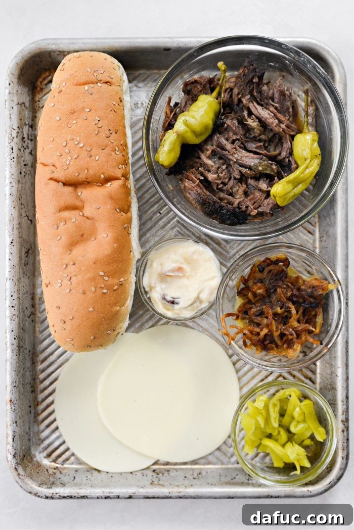 Ingredients laid out for making Mississippi Pot Roast Sandwich including a sub roll, pot roast, cheese, pepperoncini, aioli, and fried onions.
