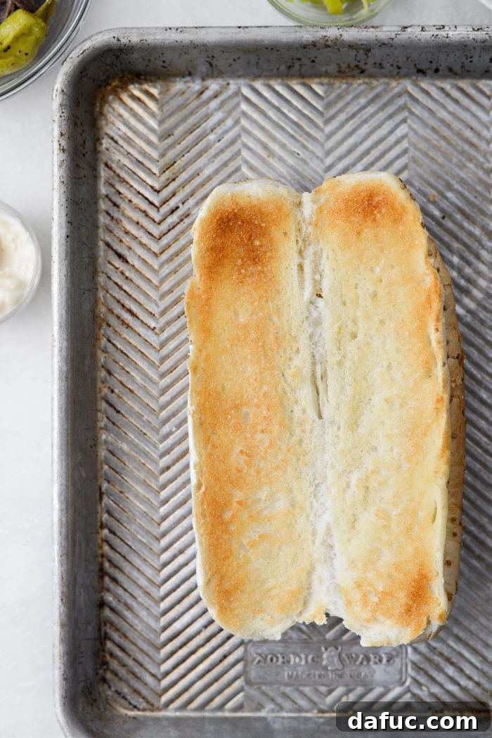A sliced sub bun, cut open and placed on a baking sheet, ready for toasting under the broiler.