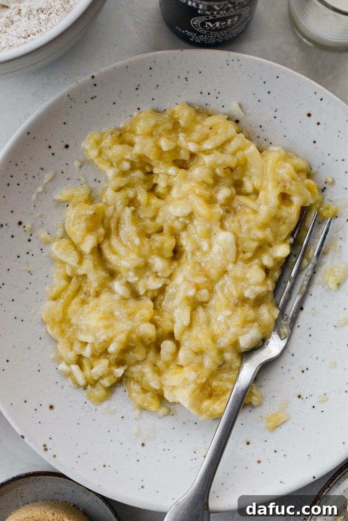 Two ripe bananas being mashed in a shallow bowl