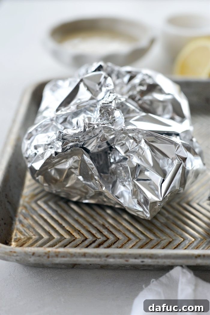 Foil parcels of beets and garlic wrapped and crimped, ready for the oven on a baking sheet