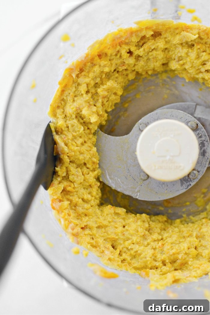 Food processor bowl with hummus being scraped down the sides for even blending