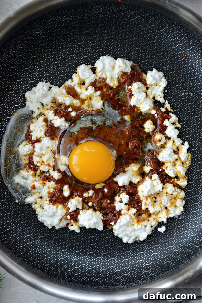 Three Delicious Feta Fried Egg Ideas 6 Cracking a Large Egg onto Pesto and Melting Feta in a Skillet