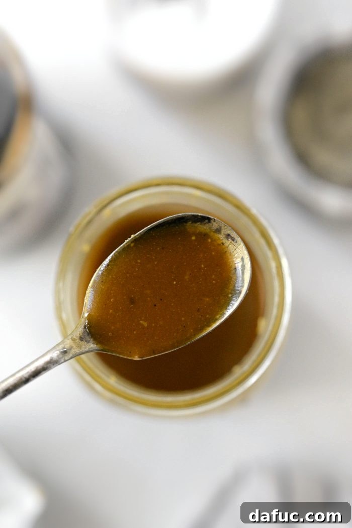 A small glass jar of homemade Balsamic Honey Dijon Vinaigrette garnished with a sprig of rosemary