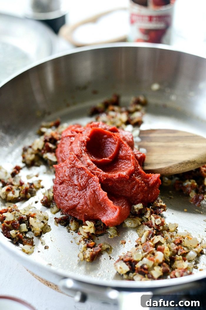 Perfect Homemade Pizza Sauce 11 Tomato paste being added to the reduced wine and herb mixture in the skillet, ready to be stirred in.