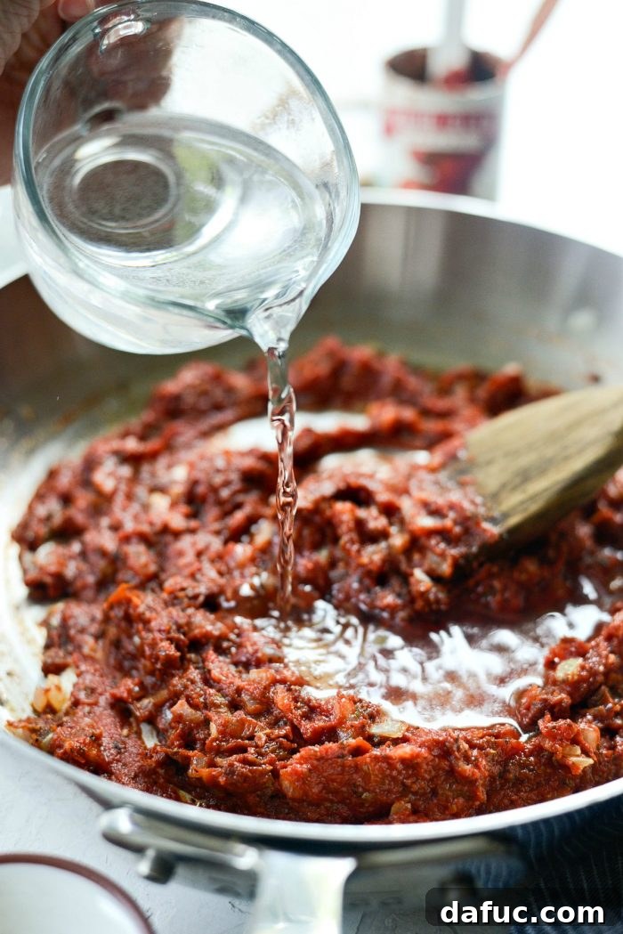 Perfect Homemade Pizza Sauce 12 Water being poured into the skillet with tomato paste and other ingredients, to create the base of the pizza sauce.