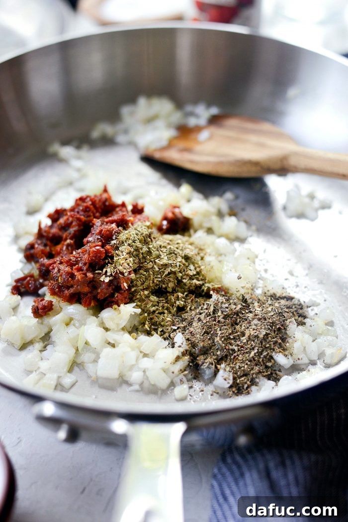 Perfect Homemade Pizza Sauce 7 Minced sun-dried tomatoes, dried oregano, and dried basil being added to the sautéed onions and garlic in a pan.