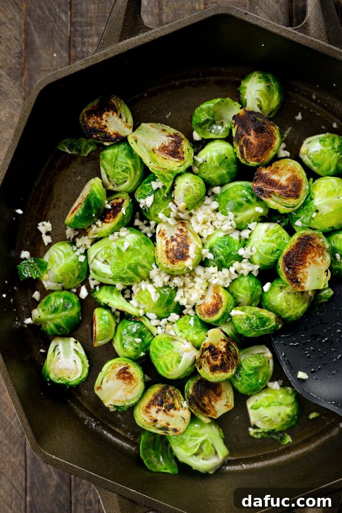 Finely chopped garlic being added to golden-brown Brussels sprouts in a skillet