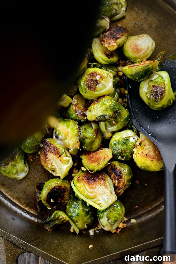 Two tablespoons of miso glaze being poured over roasted Brussels sprouts in a skillet