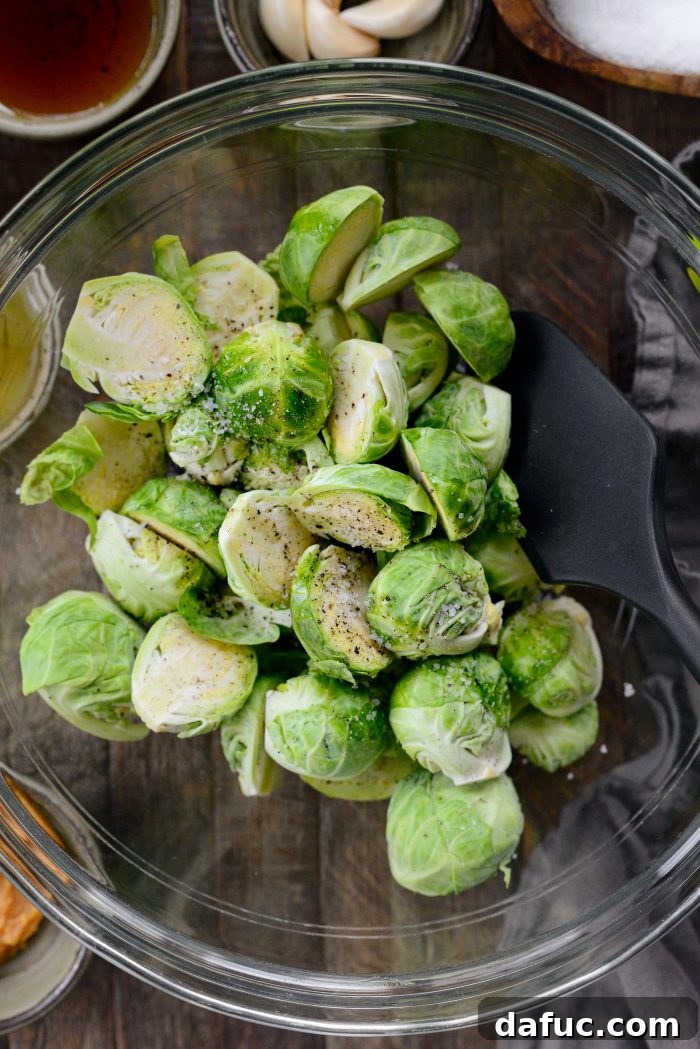 Brussels sprouts tossed with avocado oil, kosher salt, and black pepper in a bowl