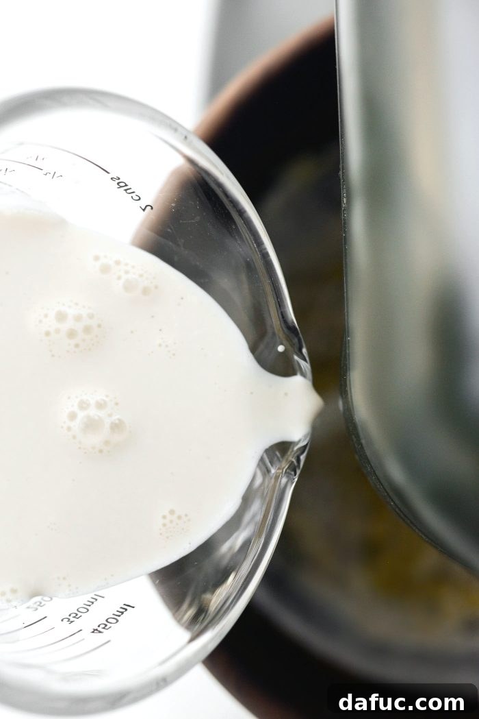 Wet ingredients being poured into the stand mixer bowl with dry ingredients