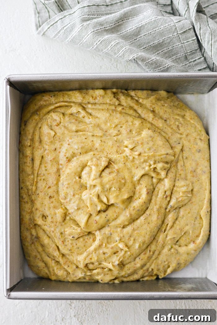 Lemon Pistachio Cake batter being spooned into a prepared square baking pan