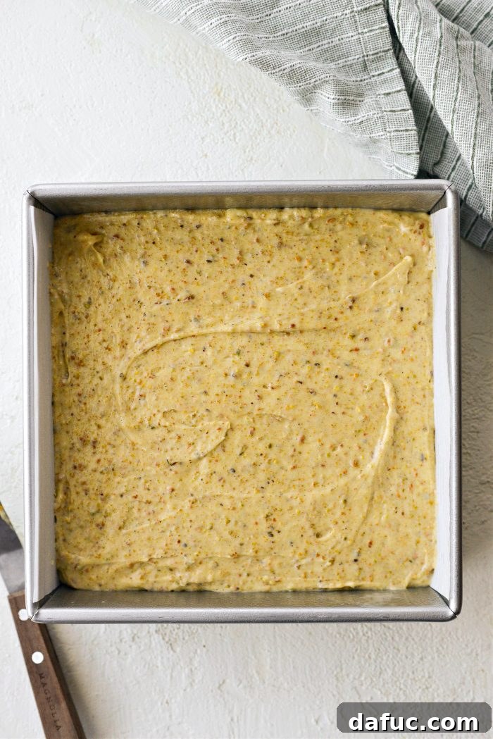Offset spatula spreading cake batter evenly in a square baking pan