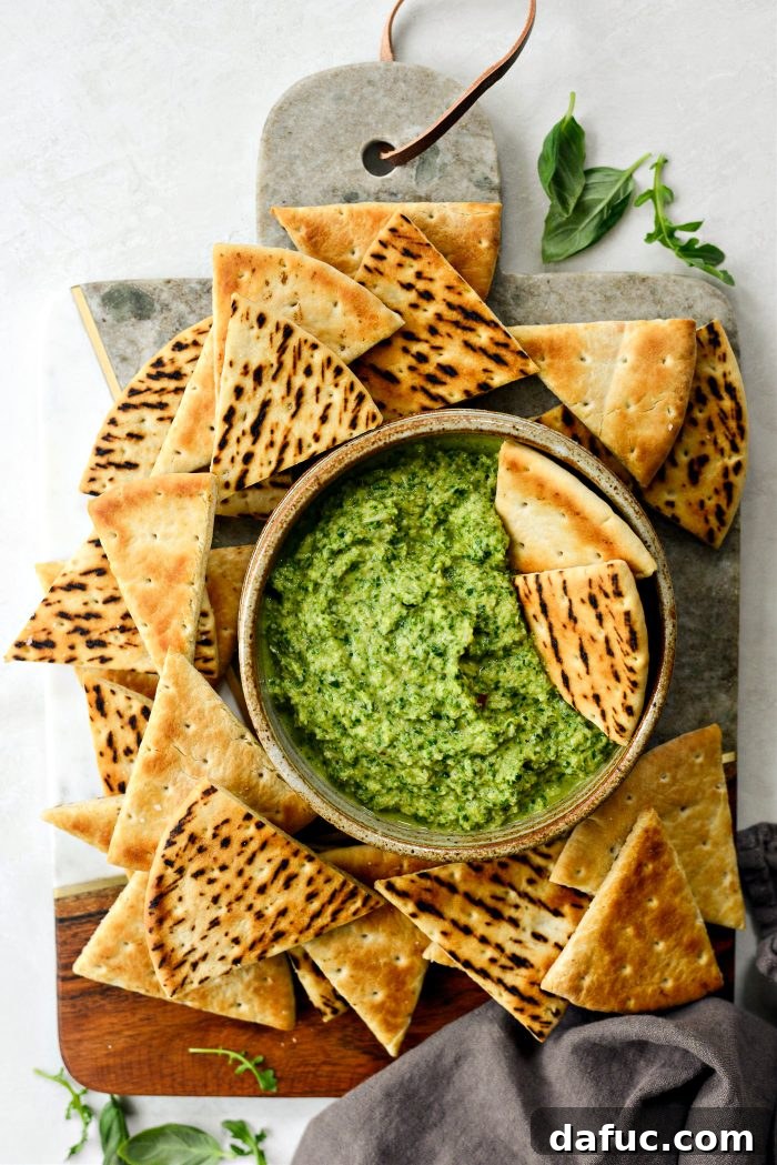 Creamy Artichoke Arugula Dip 11 A bowl of Artichoke Arugula Dip with toasted pita bread, naan, and vegetable sticks for dipping.