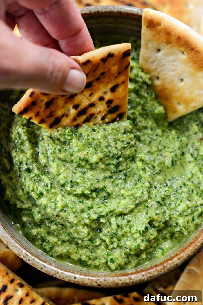 Creamy Artichoke Arugula Dip 13 A bowl of Artichoke Arugula Dip on a wooden surface, ready to be enjoyed.