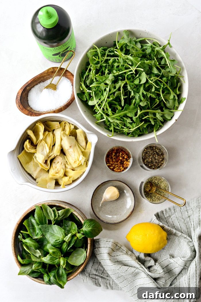 Creamy Artichoke Arugula Dip 4 Fresh ingredients laid out for making Artichoke Arugula Dip, including artichoke hearts, garlic, lemon, arugula, basil, and olive oil.