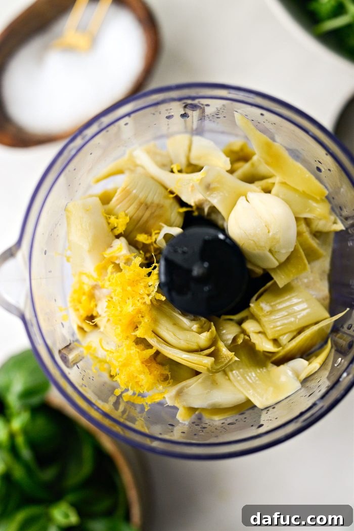 Creamy Artichoke Arugula Dip 5 Drained artichoke hearts, garlic, lemon zest, and lemon juice in a food processor bowl.