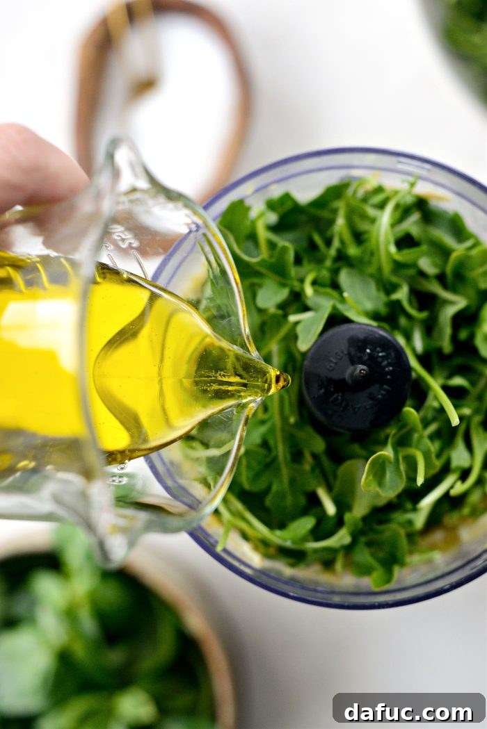 Creamy Artichoke Arugula Dip 7 Pouring olive oil into the food processor with the other ingredients.