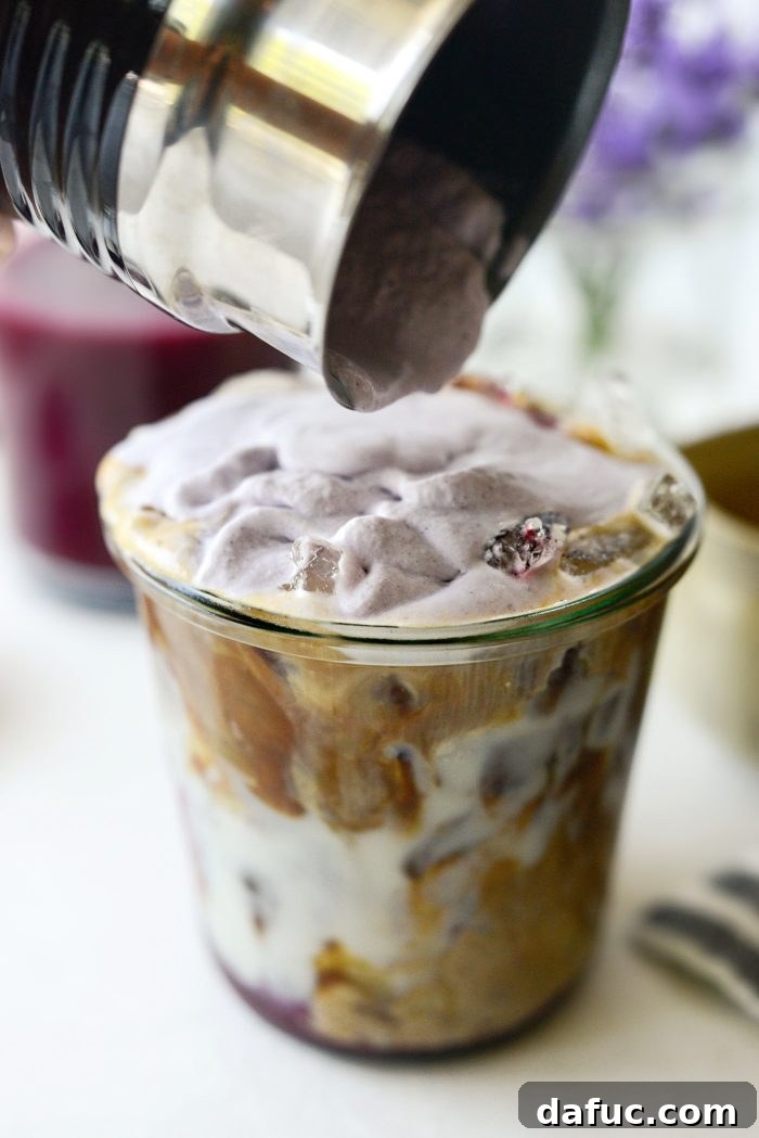 Pouring blueberry cold foam onto iced latte