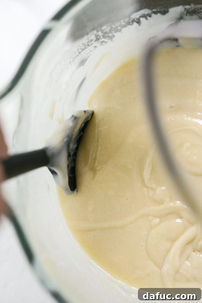 Scraping down the sides of the mixer bowl to ensure all batter is mixed.